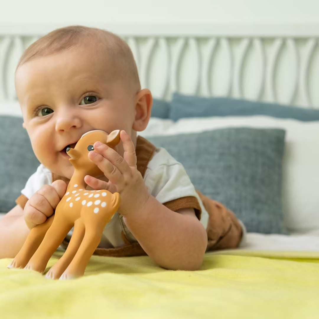 Baby playing with fan fan teh toy deer teething toy on a bed