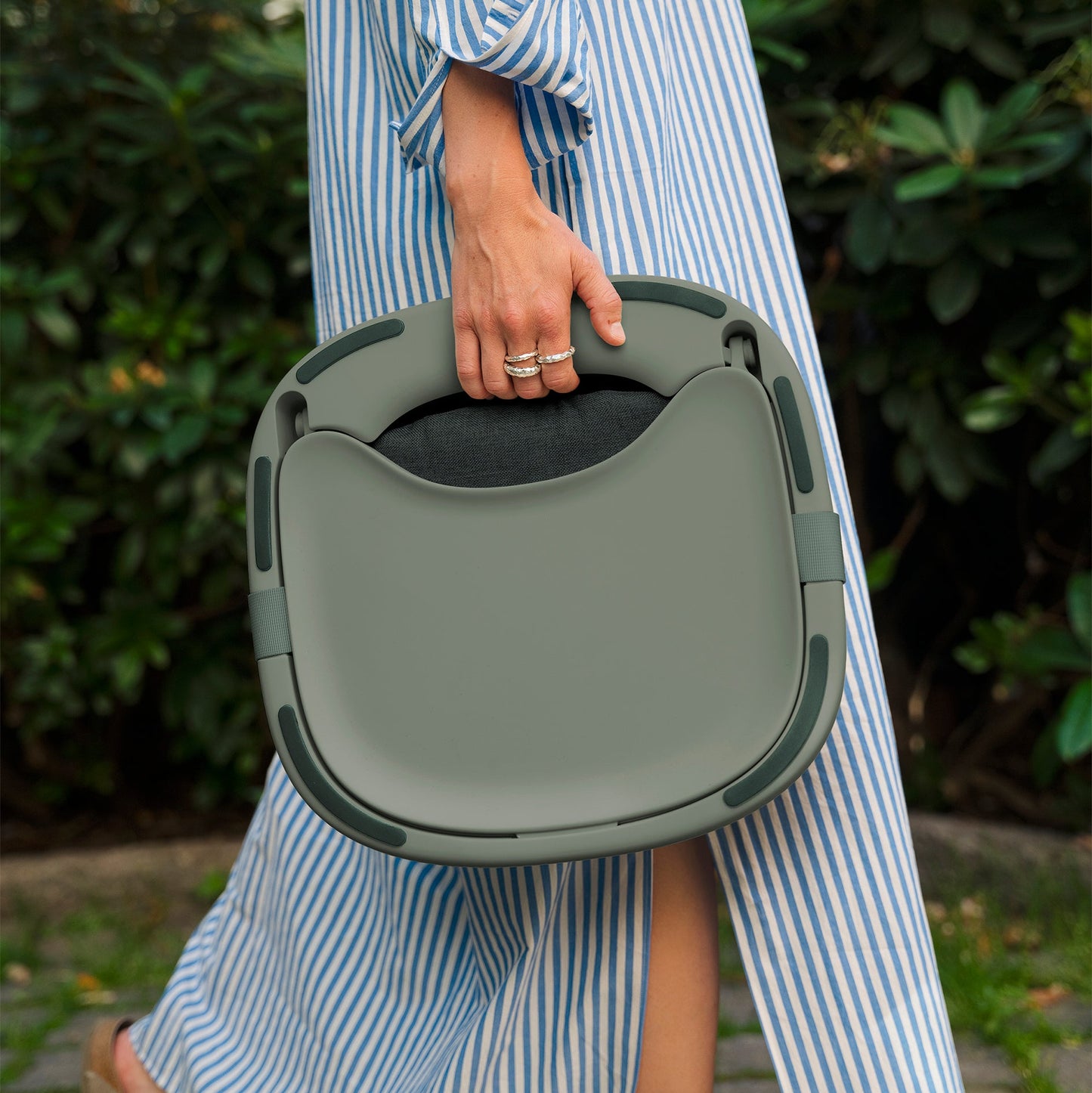 Person holding a green baby highchair portable outdoors with a blurred background