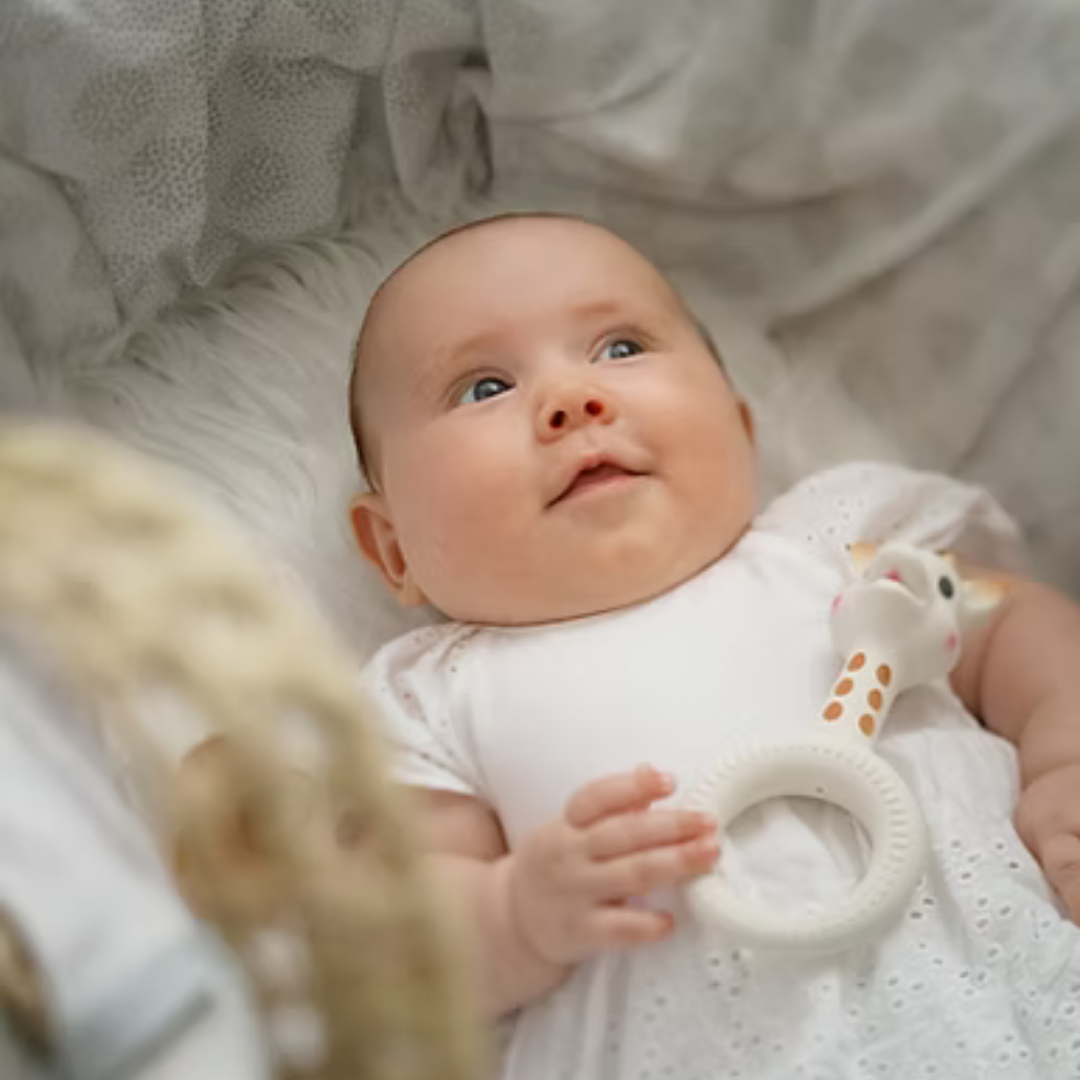 Baby lying on a soft surface holding a Sophie la Girafe So pure teething ring