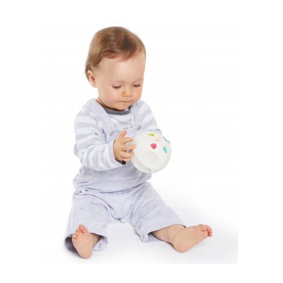 Baby in grey outfit holding a colourful toy ball on a white background