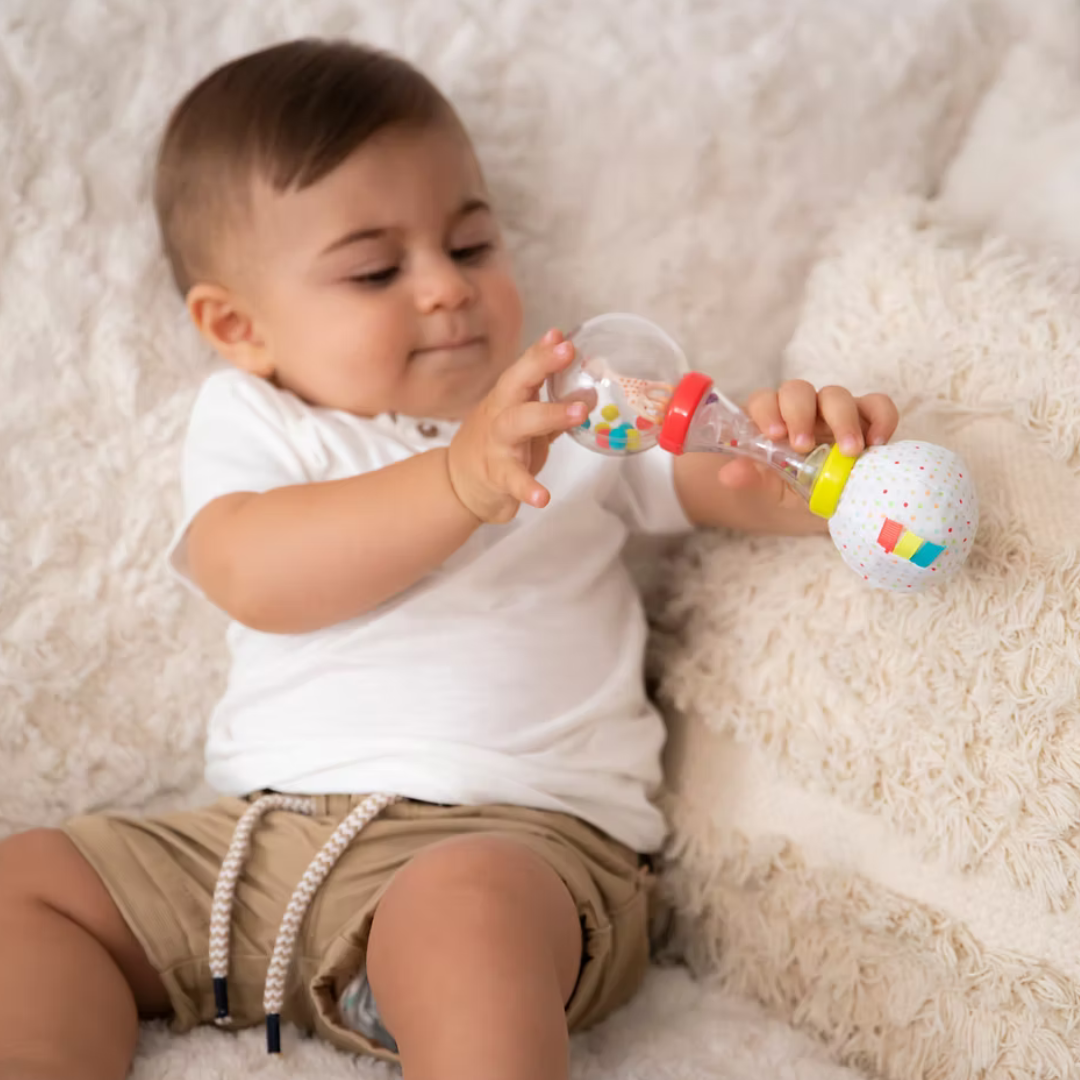 Child playing with a colorful Sophie la giraffe soft maraca toy on a soft surface
