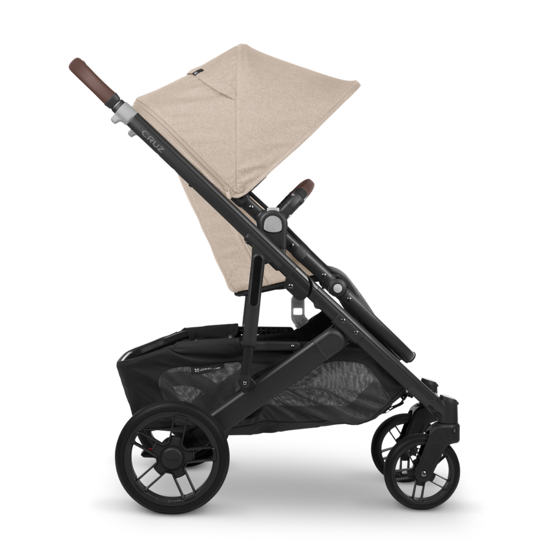 UPPAbaby Cruz V2 stroller. Oat fabric, Carbon Frame and Chestnut Leather accents on handle bar and bumper bar. Side on.