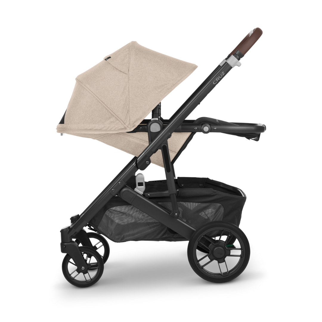 UPPAbaby Cruz V2 stroller. Oat fabric, Carbon Frame and Chestnut Leather accents on handle bar and bumper bar. Side on.