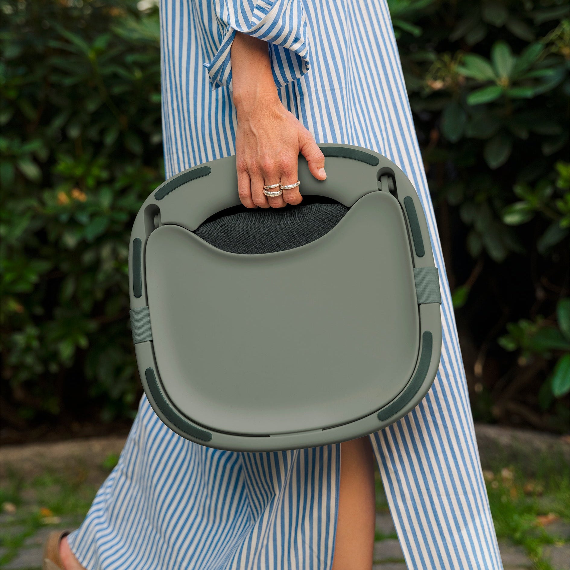 Person holding a green baby highchair portable outdoors with a blurred background
