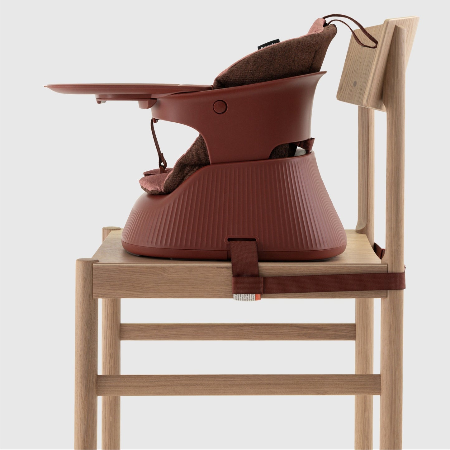 Mahogany Red portable high chair with cushion insert and tray strapped to a wooden chair on a white background. 