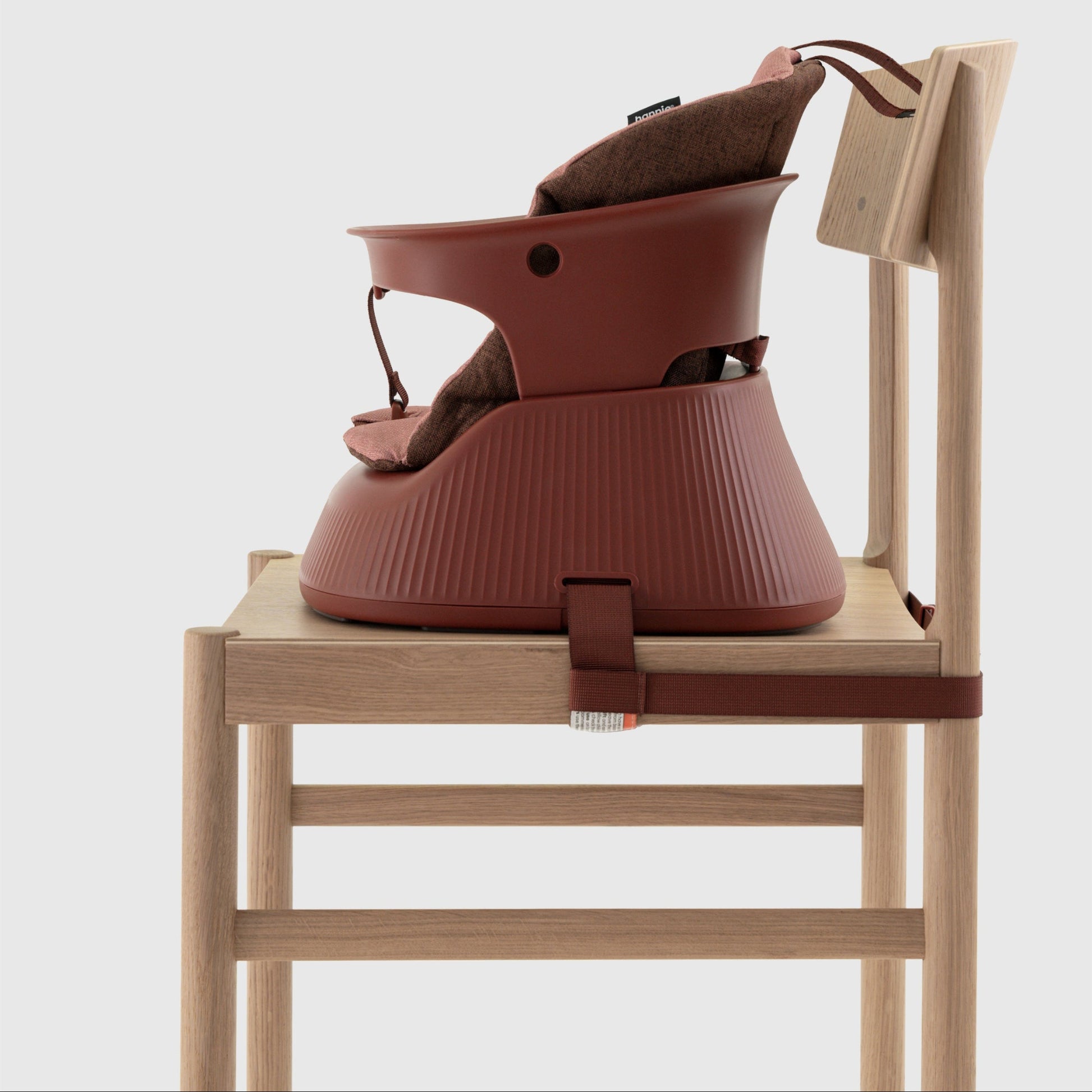 Mahogany Red portable high chair with cushion insert strapped to a wooden chair on a white background. 