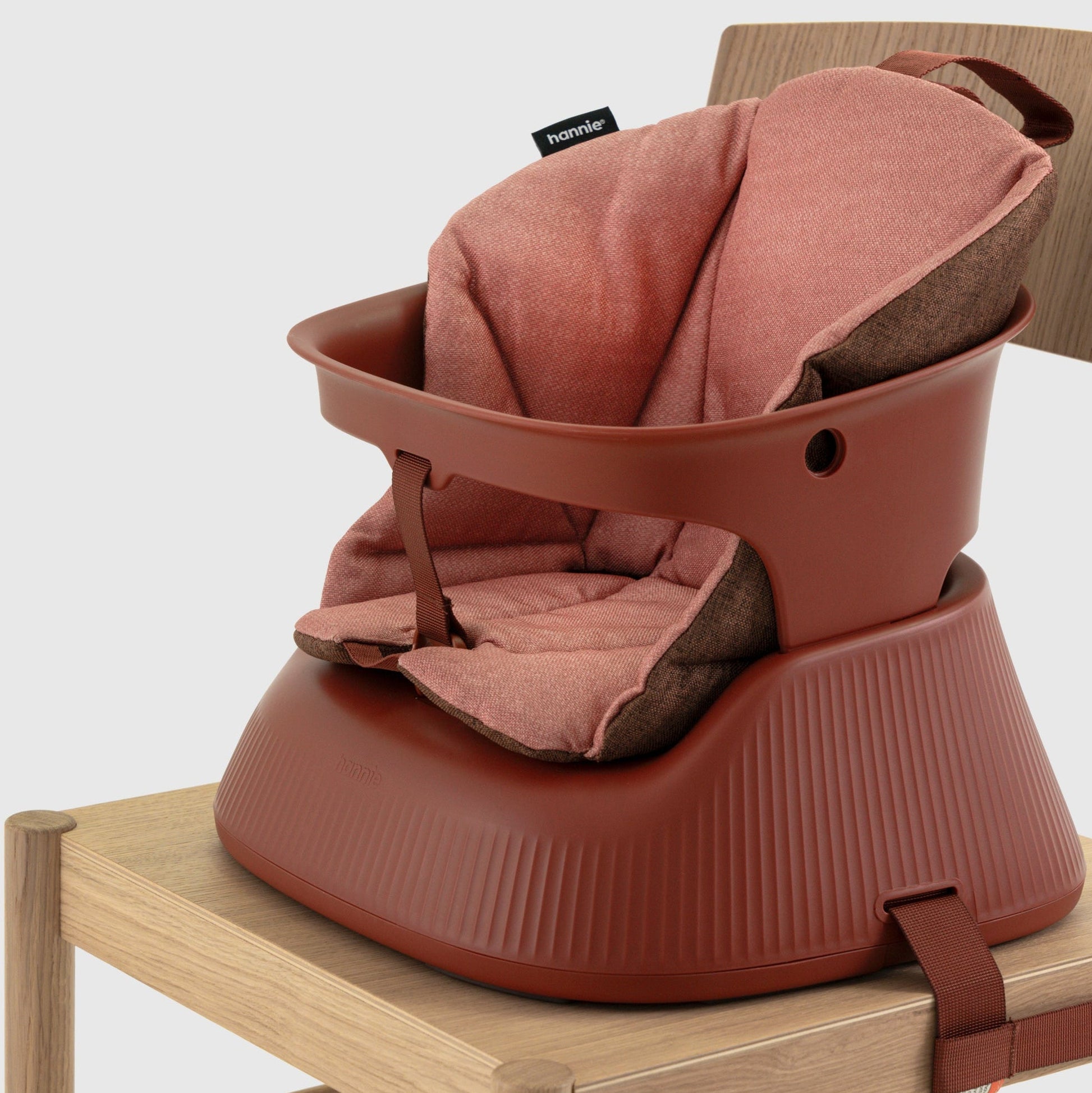 Mahogany Red portable high chair with cushion insert strapped to a wooden chair on a white background. 