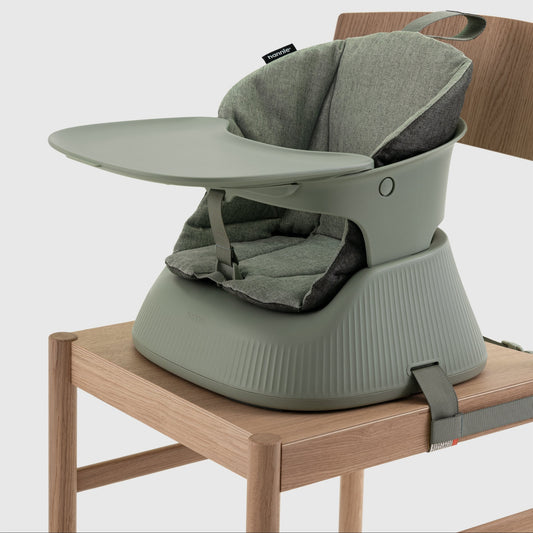 Green baby highchair with green cushion on a wooden chair with a white background
