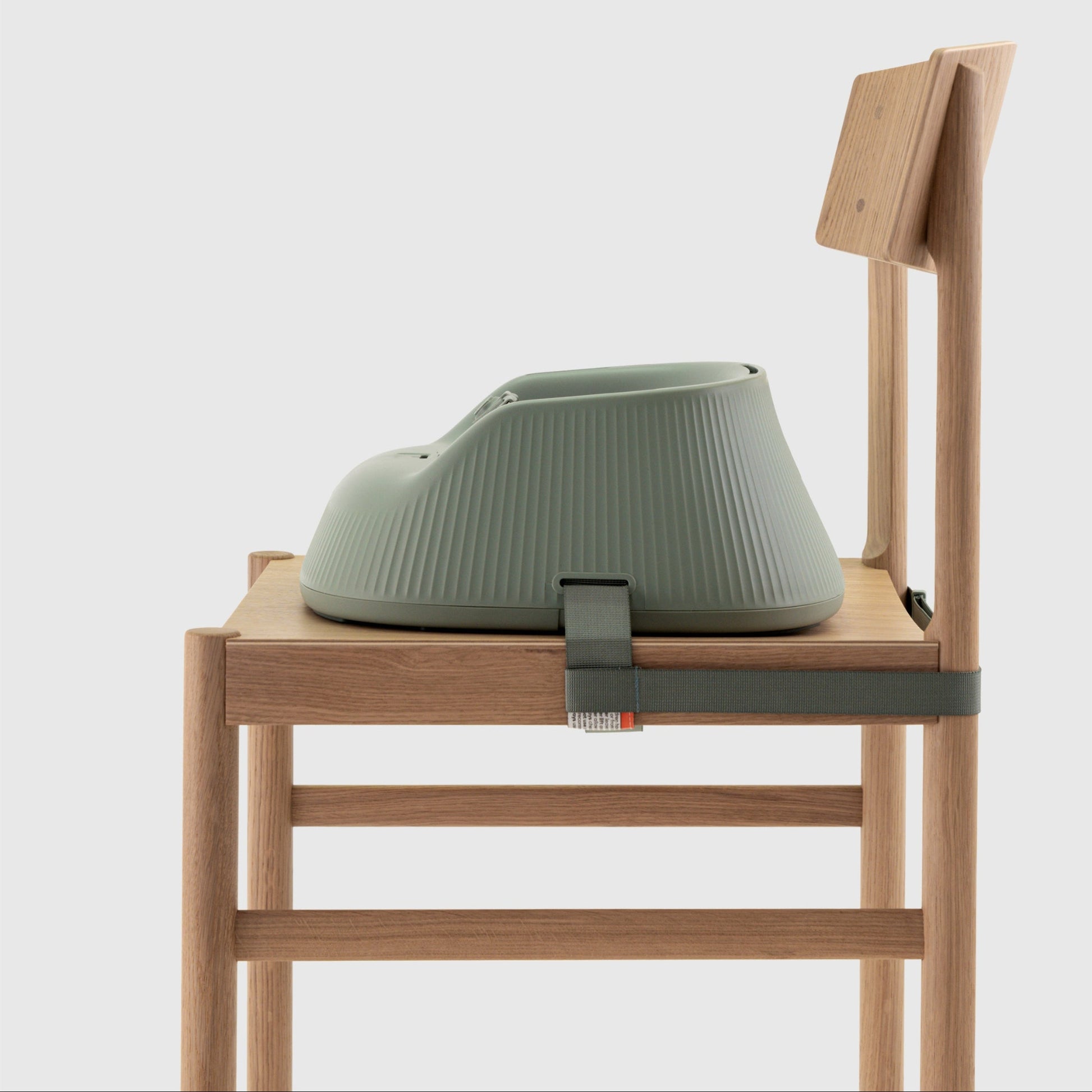 Green baby highchair seat attached to a wooden chair on a white background. 