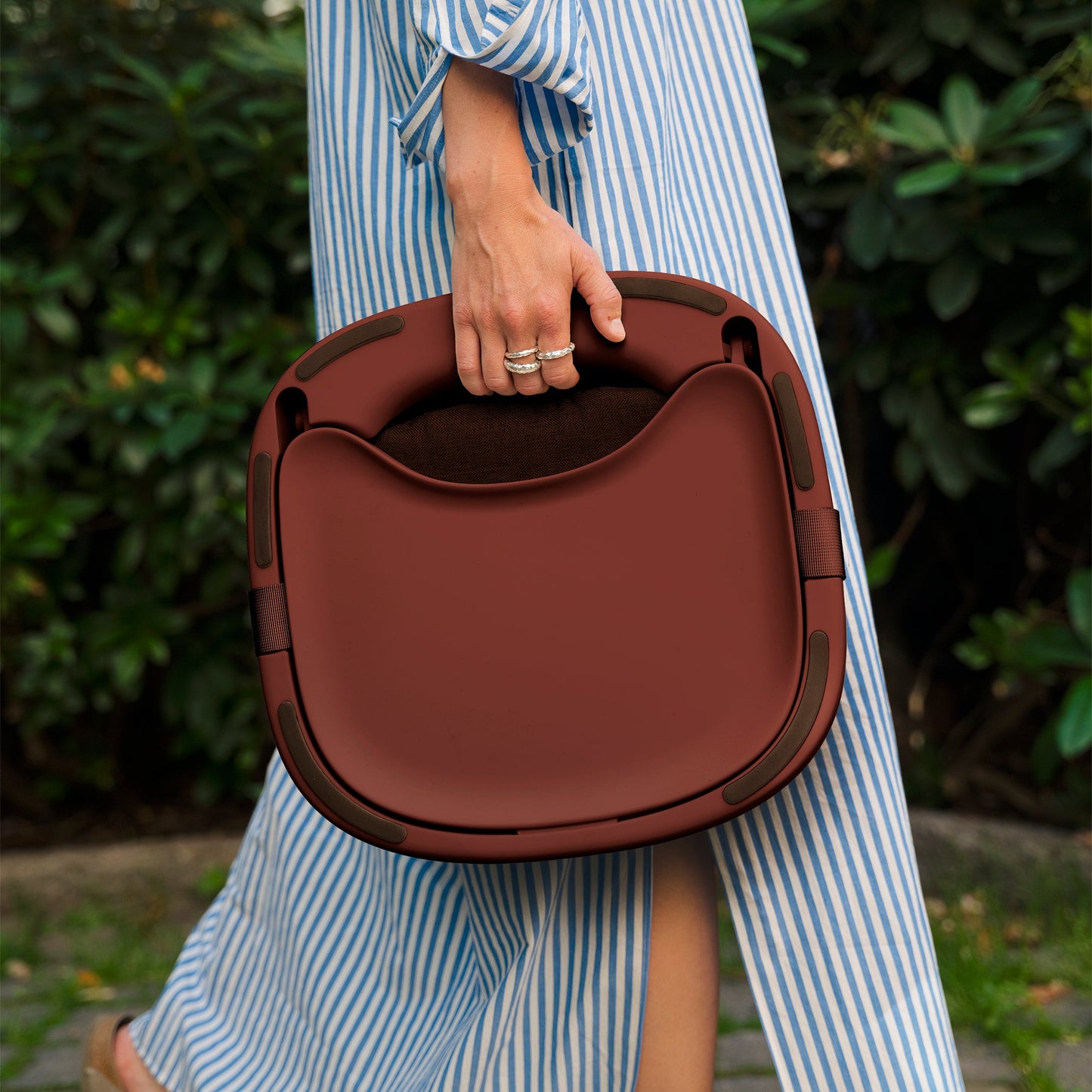person holding mahogany red portable highchair on a green back ground. 