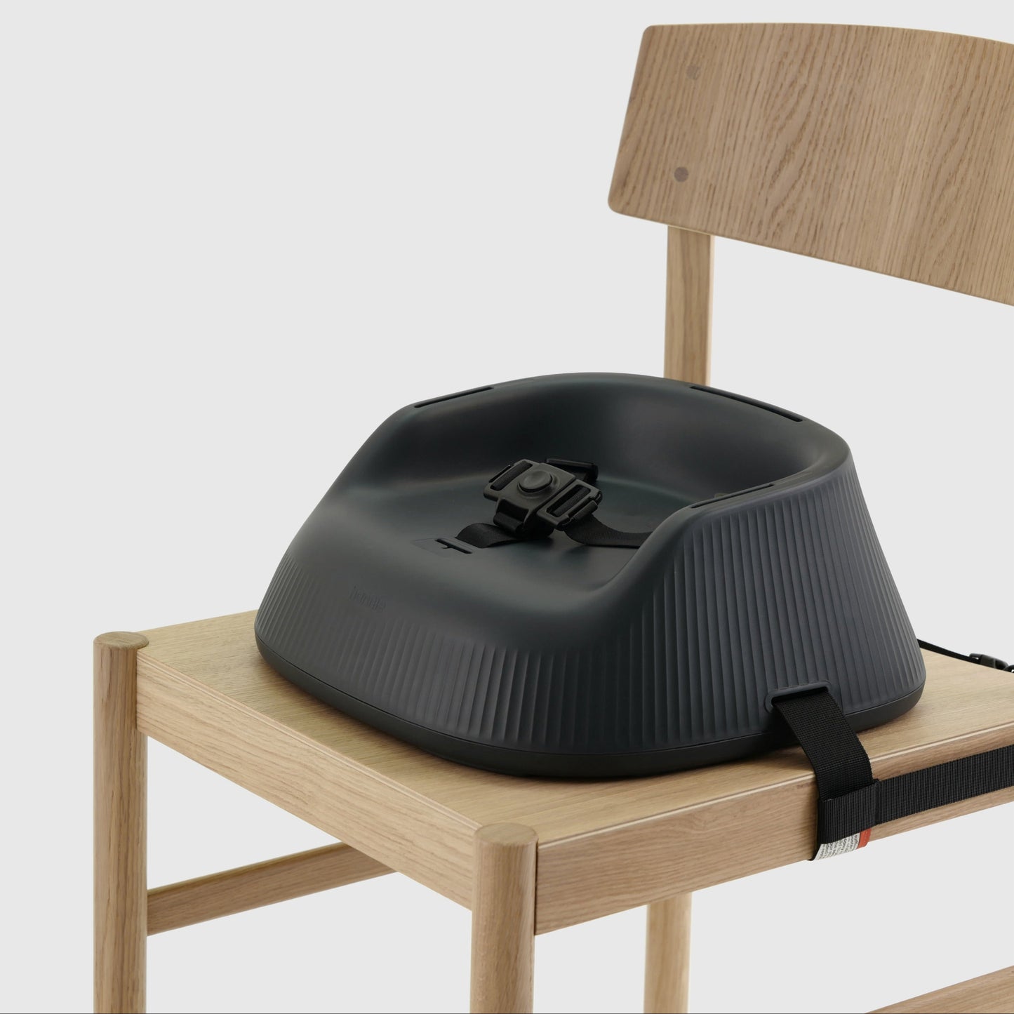 Charcoal Black portable baby highchair with grey cushion strapped to a wooden chair on a white background. 