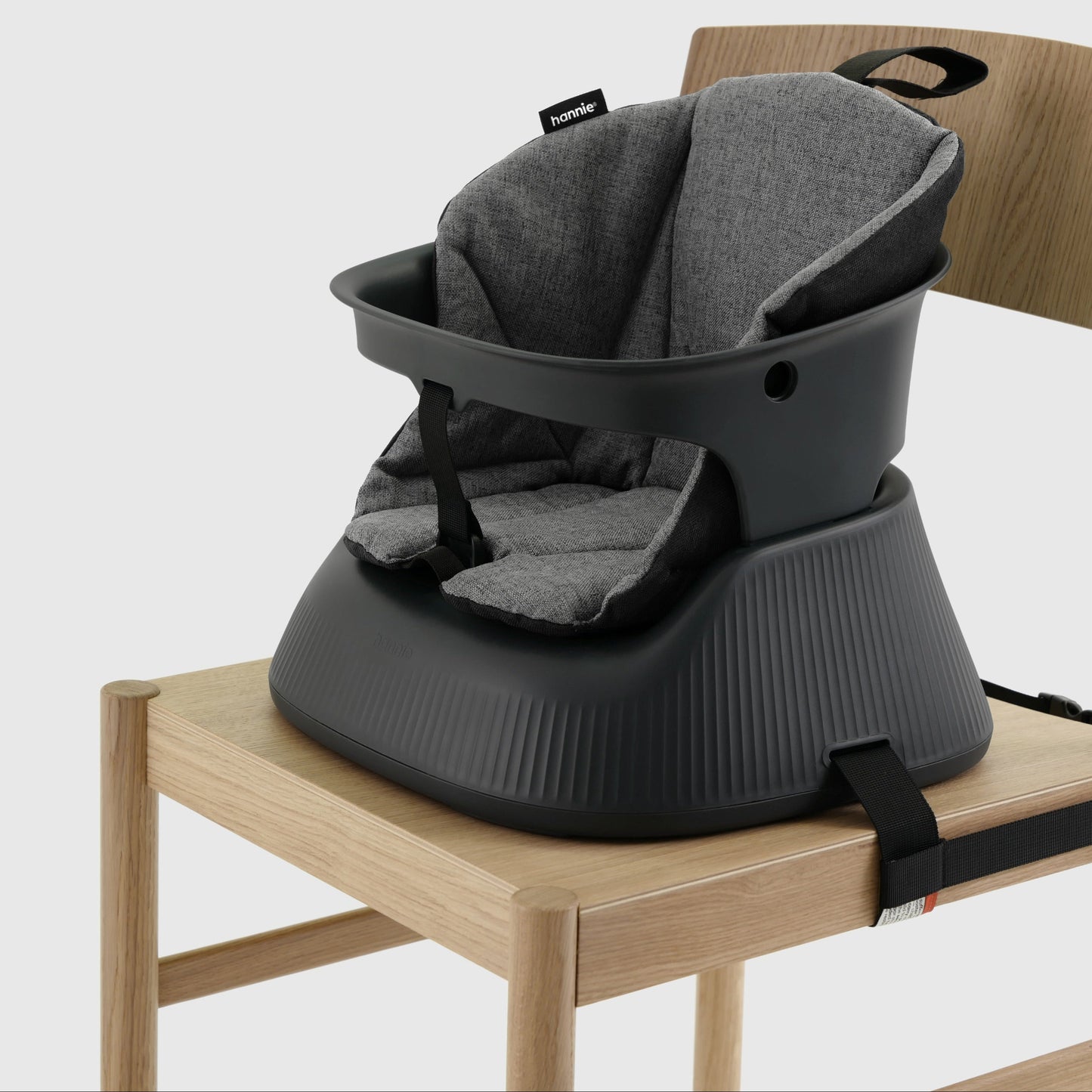 Charcoal Black portable baby highchair with grey cushion strapped to a wooden chair on a white background. 