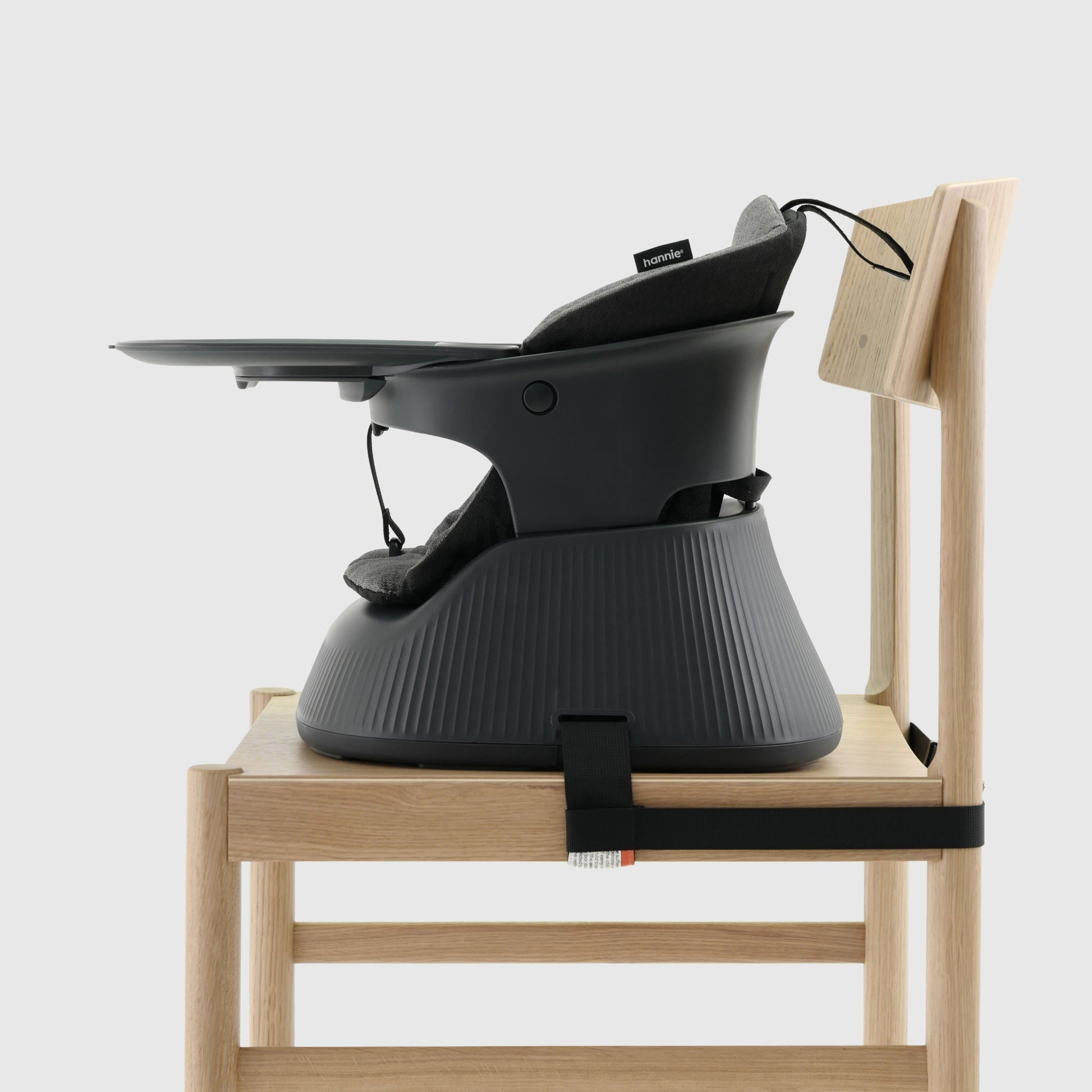 Charcoal Black portable baby highchair with grey cushion and tray strapped to a wooden chair on a white background. 