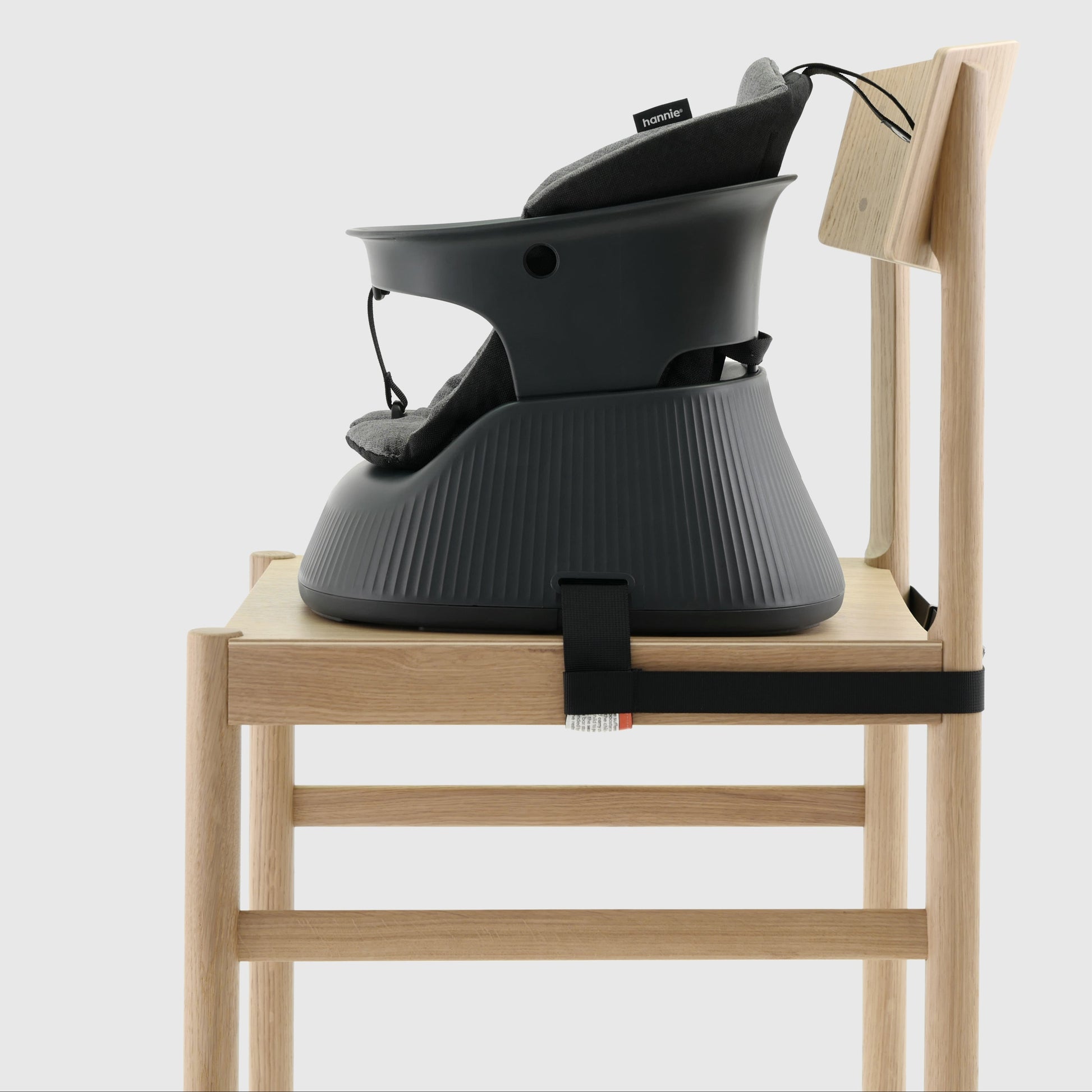 Charcoal Black portable baby highchair with grey cushion strapped to a wooden chair on a white background. 