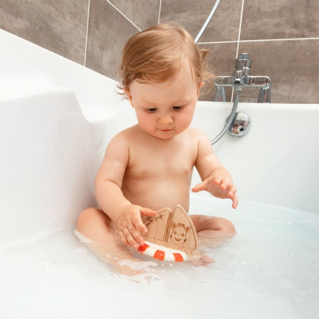 baby in bath playing with wood boat toy with ring and giraffe picture on the wood.