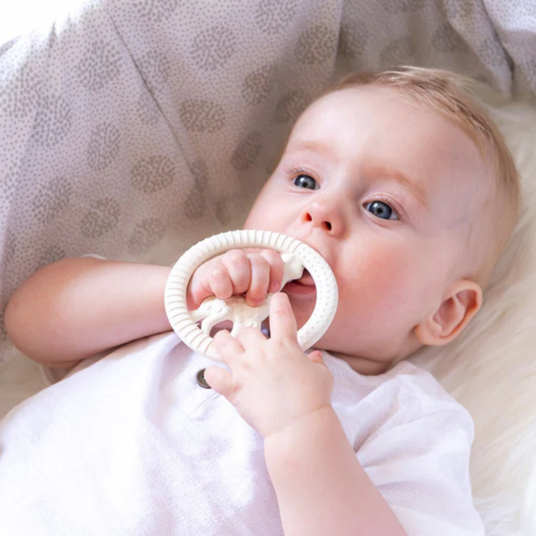 Baby holding a white teething ring with a soft blanket in the background