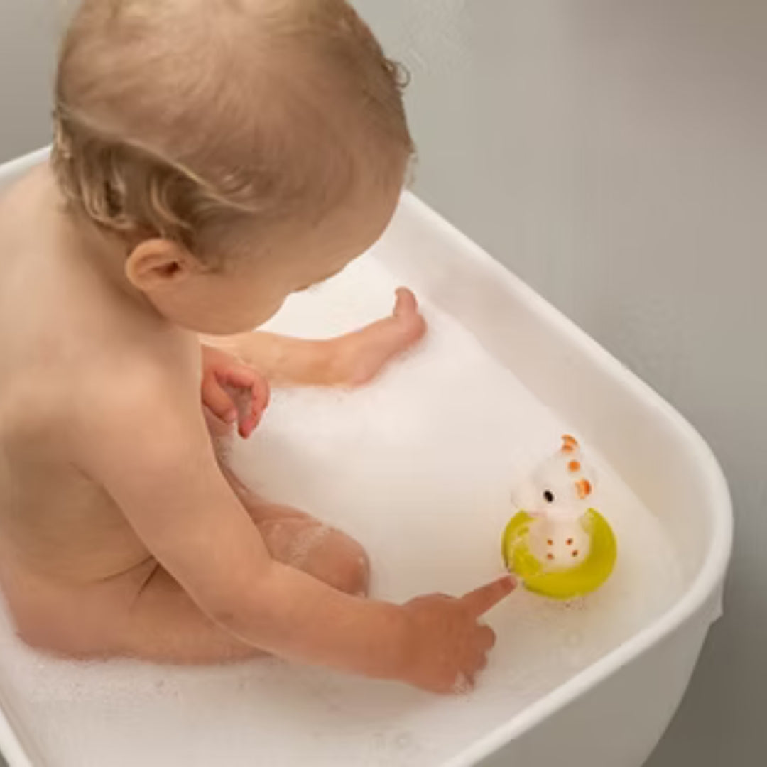 Baby playing with a  Sophie la girafe toy with yellow ring  in a bathtub
