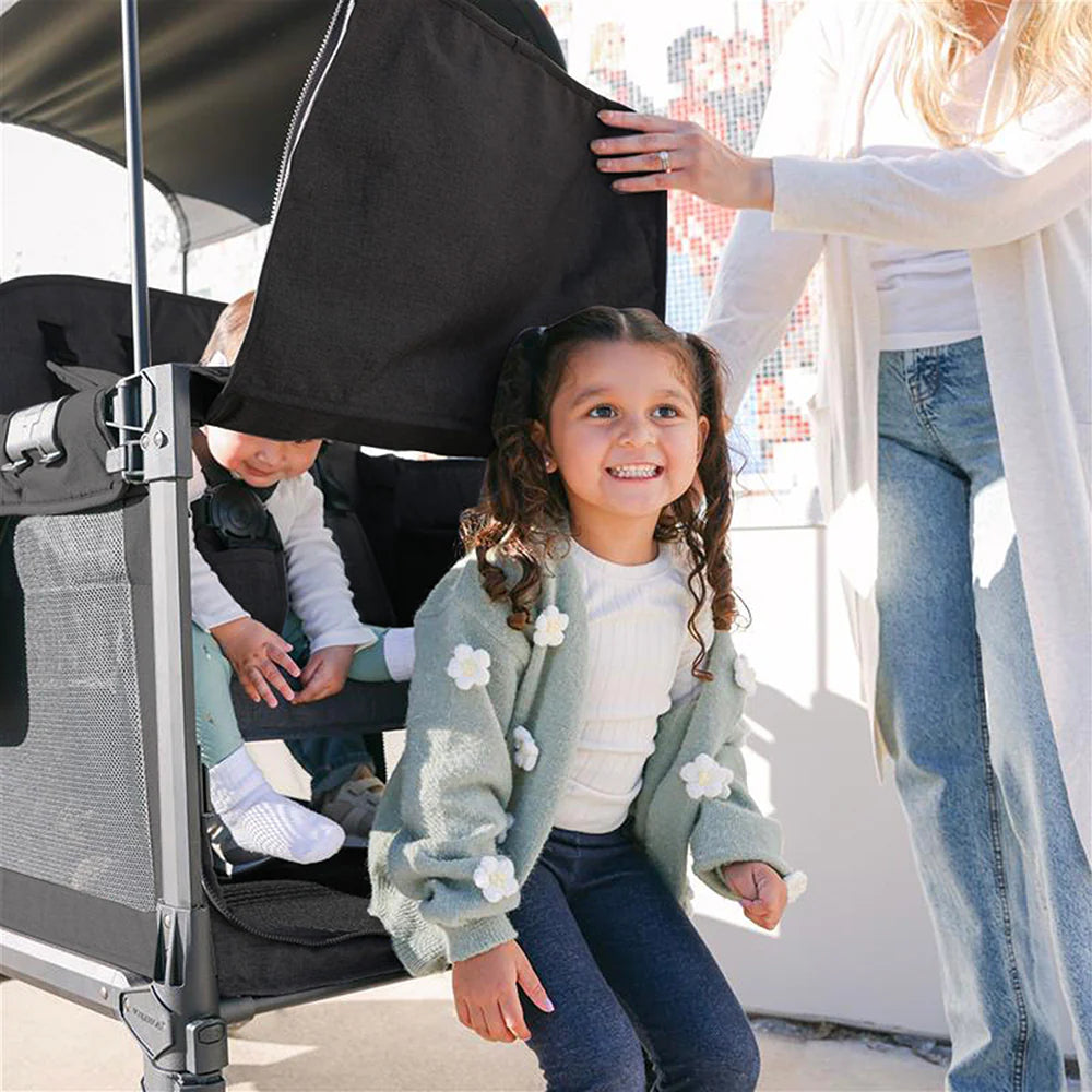 Child climbing out of the Wonderold black stroller wagon with baby strapped in behind. 